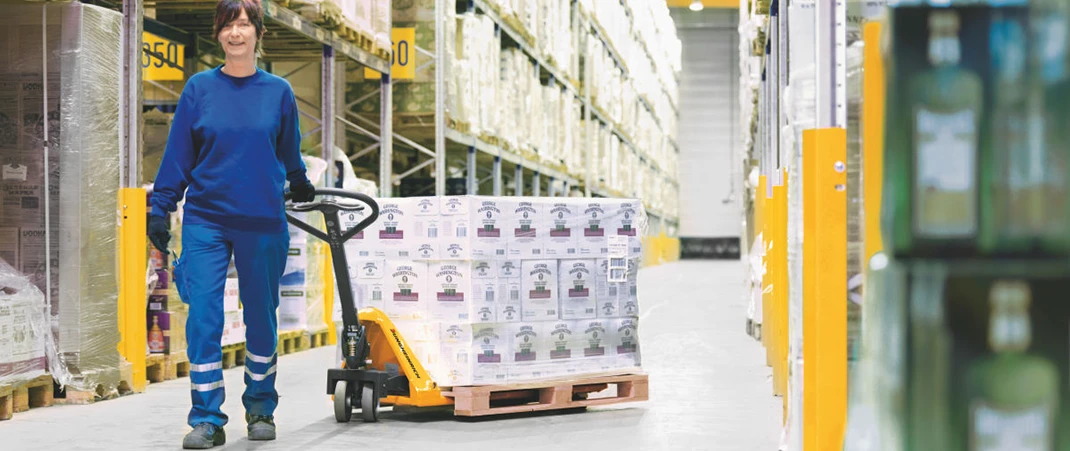 Eine Frau transportiert eine beladene Palette mithilfe eines Handhubwagens