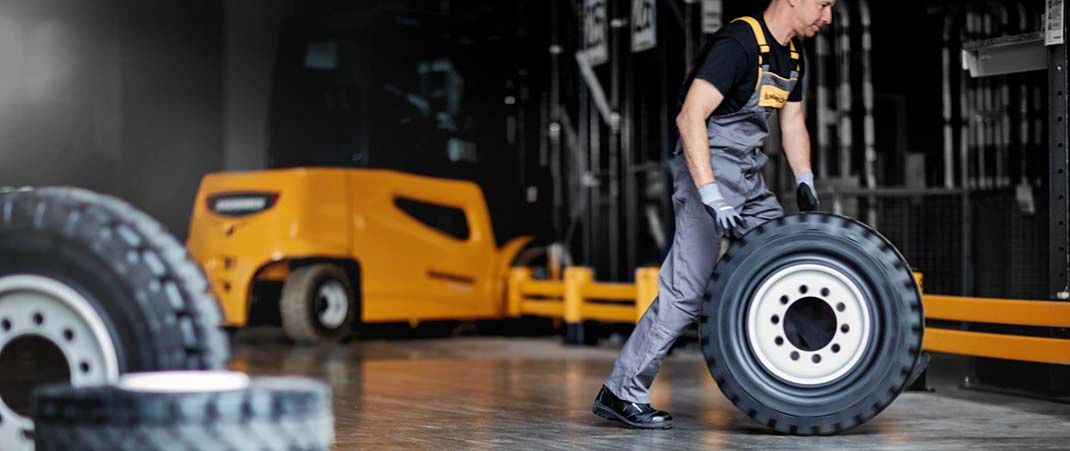 Mann rollt einen Gabelstaplerreifen durch eine Lagerhalle